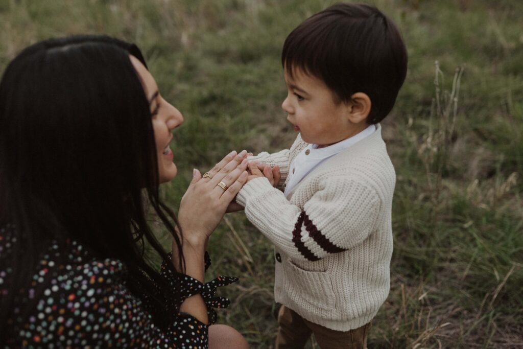 Mom holding son's hands and smiling at him during their Texas hill country family photos.