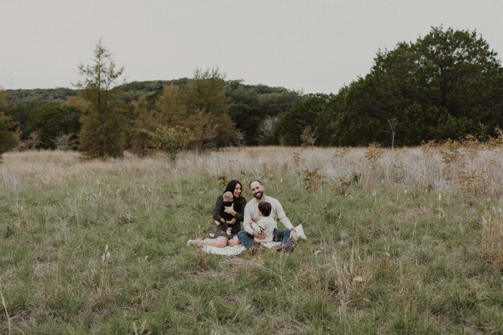 Family sitting on a blanket in a field during their Texas hill country family photos.