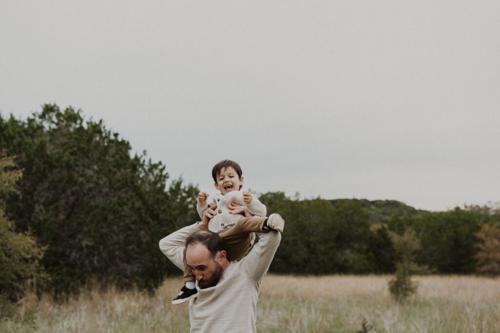 Toddler riding on Dad's shoulders and laughing during their Texas hill country family photos.